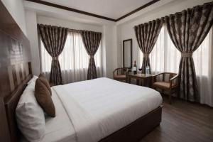 a bedroom with a white bed and a desk and windows at Hotel Rana Taradevi in Shimla