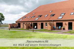 a building with a red roof with windows at Ferienwohnung Freia - Gulfhof nahe Greetsiel mit Sauna, Garten & 3 Schlafzimmern in Krummhörn