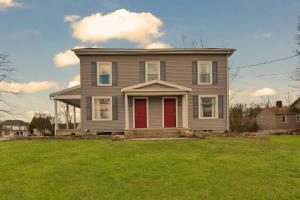 a house with a red door on a green lawn at The John Collins House in Canfield