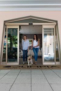 Dos mujeres y un perro parados en una puerta en Olimpia Hotel & Aparthotel en Bibione