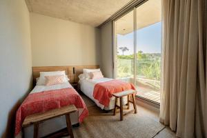 two beds in a room with a large window at CasaChica Hotel in José Ignacio