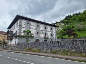 a white building with a stone wall next to a road at Hostal Betelu in Betelu