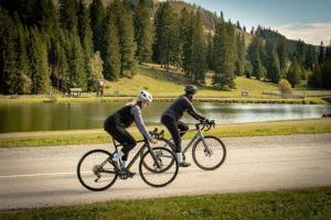 two people riding bikes on a road next to a lake at Almenlandhof in Fladnitz an der Teichalm