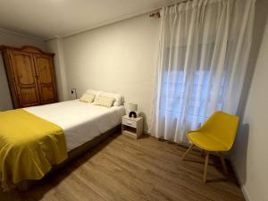 a bedroom with a bed and a yellow chair and a window at Siente Riaño in Riaño