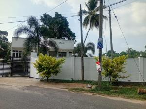 a white building with a fence and palm trees at Omik Residence in Dinapamunuwa