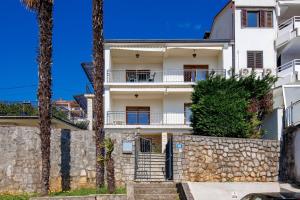 a white house with a stone wall and palm trees at Maestro Apartments Ičići Opatija Riviera in Ičići