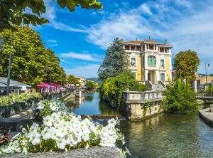 a river in a city with a building and flowers at Mon nid sous les toits in L'Isle-sur-la-Sorgue