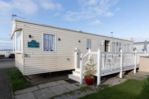 a white tiny house with a porch and a sign on it at 3 Bedroom Caravan, Edi Rita, Robin Hood, Pet Friendly in Meliden