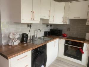 a kitchen with white cabinets and a sink and a dishwasher at Chambers Cottage in Drumellihy +3 photos