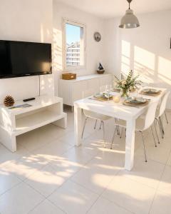 a white dining room with a white table and a tv at L Echappee Jardin prive proche plage Sainte Cecile in Camiers