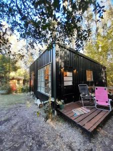 a black tiny house with a deck and two chairs at La Chaira in Santa Ana