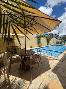a table and chairs under an umbrella next to a pool at Encanto Parangaba in Fortaleza