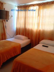 two beds in a hotel room with orange curtains at Hotel Avenida El Bosque a 2 cuadras de la clínica foscal y cardiovascular,HIC,Unab in Floridablanca +2 photos