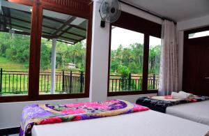 two beds in a room with a balcony with windows at Ella River Breeze Homestay in Ella