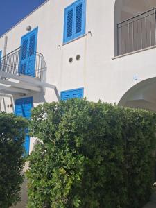 a white building with blue windows and a bush at Macari Residence Central Apartment in Macari