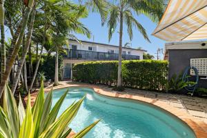 a swimming pool with palm trees and a building at Beachcomber Peregian Beach in Peregian Beach