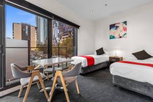 a hotel room with two beds and a table and chairs at Comfort Apartments on Elizabeth in Melbourne