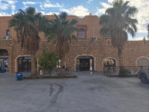 a brick building with palm trees in front of it at Hotel El Golla in Er Rachidia