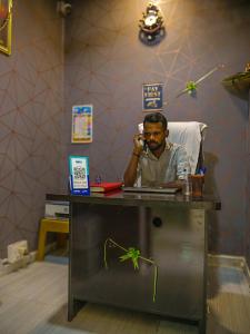 a man sitting at a desk talking on a cell phone at Hotel GK Lodging & Boarding in Khāpri