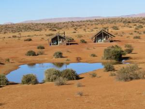 two huts in the middle of a field with a pond at Tented Camp in Augrabies in Kakamas