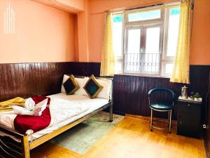 a bedroom with a bed and a chair and a window at PEMA Hotel VSTM in Darjeeling +13 photos