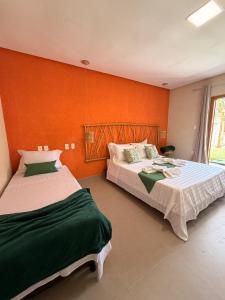 two beds in a room with an orange wall at Pousada Verdes dos Corais in São Miguel dos Milagres