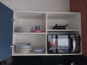 a cupboard with plates and a microwave in a kitchen at QUINTAL DE BÚZIOS- casa com piscina e 3 suítes completas in Búzios