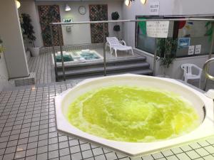 a bath tub filled with green liquid on a tiled floor at Capsule&Spa Grand Sauna Hiroshima (Male Only) in Hiroshima