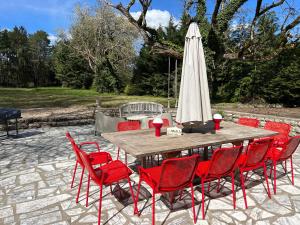 a wooden table with red chairs and an umbrella at Gîte la plotuère in Gy-en-Sologne