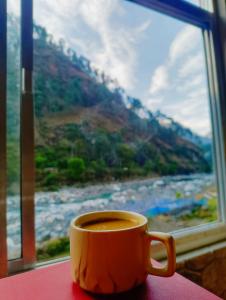 a cup of coffee sitting on a table in front of a window at Ganga Kinaare Homestay in Uttarkāshi