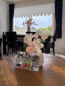a table with a vase with flowers and a magazine at Appartementen Koets in Biggekerke