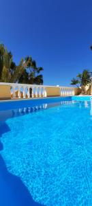 a blue swimming pool with white chairs and palm trees at Casa Panorama in La Pared