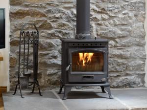 a stove in front of a stone wall at Sgubor Ucha in Trefriw