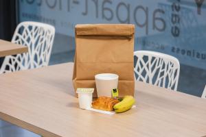 a paper bag and a banana and cups on a table at Appart'City Classic Toulouse Tournefeuille in Tournefeuille