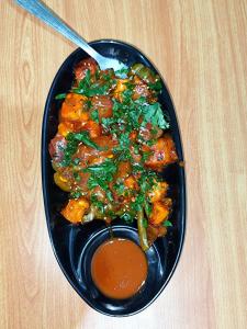 a black plate of food with sauce on a table at Jim Corbett Guest House in Jhirna