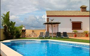 una piscina frente a una casa con sillas y sombrilla en Chalet Vigía 113, en Conil de la Frontera