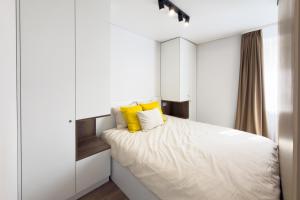 a white bedroom with a bed with yellow pillows at AC Vienibas Square apartments in Daugavpils