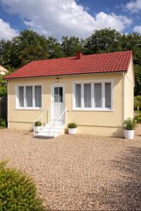 a yellow house with a red roof on a gravel driveway at Maison prairie en fleurs in Le Perray-en-Yvelines