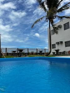 a blue swimming pool next to a building with a palm tree at Pousada Sol Nascente in Mucuri