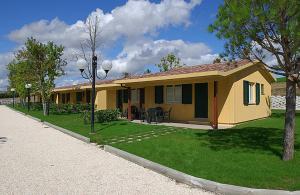 a small yellow house with a grass yard and a street at Centro Vacanze Verde Azzurro in Cingoli
