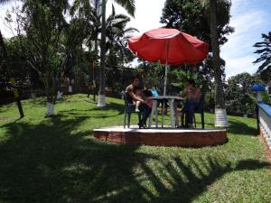three people sitting at a table under a red umbrella at Finca La Piscina in Viterbo