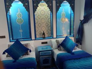 two twin beds in a room with blue windows at Dar Achraf in Chefchaouen