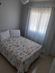 a bedroom with a bed with a flowered blanket and a window at Ap 503 Ed Brisa do sol em Piratuba in Piratuba +20 photos