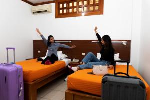 two women sitting on beds with their arms in the air at Hostal Macaw in Guayaquil