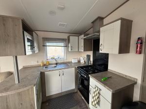 a kitchen with white cabinets and a stove top oven at Oakley caravan rental in Skegness