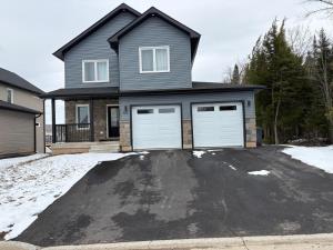 a house with two white garage doors on a driveway at Richies Place Modern 2BR, Parking & Private Entry in Fredericton