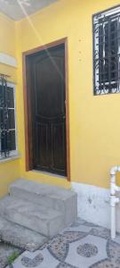 a yellow building with a black door and a window at Apartamento INRU in Puerto Cortés
