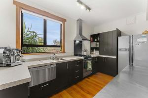 a kitchen with black cabinets and a stainless steel refrigerator at Cabbage Tree Cottage in Papamoa