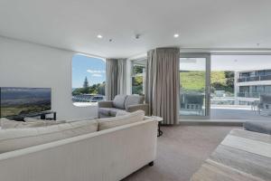 a living room with white furniture and large windows at Oceanside Belle in Mount Maunganui