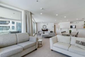 a living room with two white couches and a kitchen at Oceanside Belle in Mount Maunganui